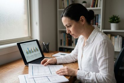 Femme analysant des tableaux financiers prévisionnels sur bureau en bois avec ordinateur portable affichant des graphiques