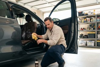 Homme appliquant un produit conditionneur sur siège en cuir de voiture avant un long voyage