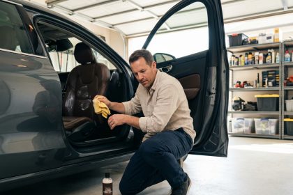 Homme appliquant un produit conditionneur sur siège en cuir de voiture avant un long voyage